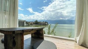 Una habitación con mesa y banco de madera, un ventanal con vista a un cuerpo de agua y edificios a lo lejos.