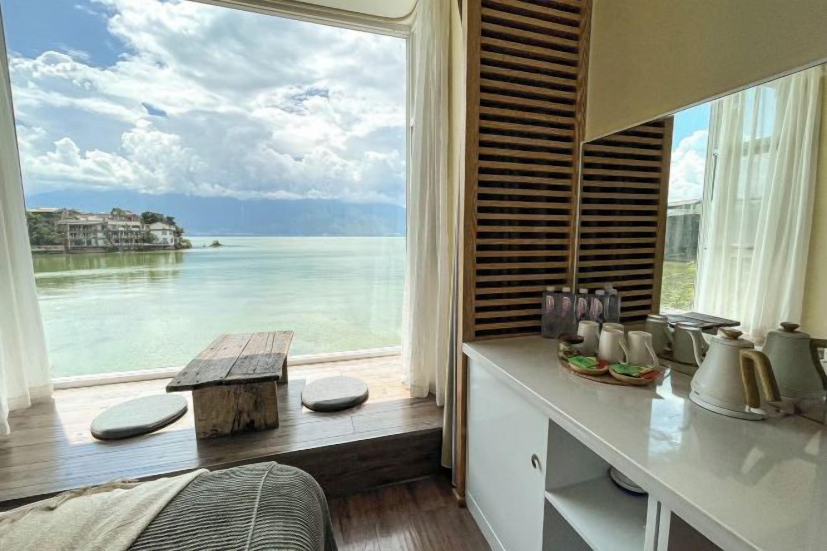 Una habitación con vista a un cuerpo de agua, una banca de madera, una mesa de comedor con platos y una encimera de cocina con utensilios.
