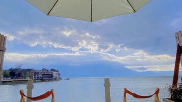 Vista al mar con cielo despejado, dos sillas de madera bajo una sombrilla blanca y un mar tranquilo.
