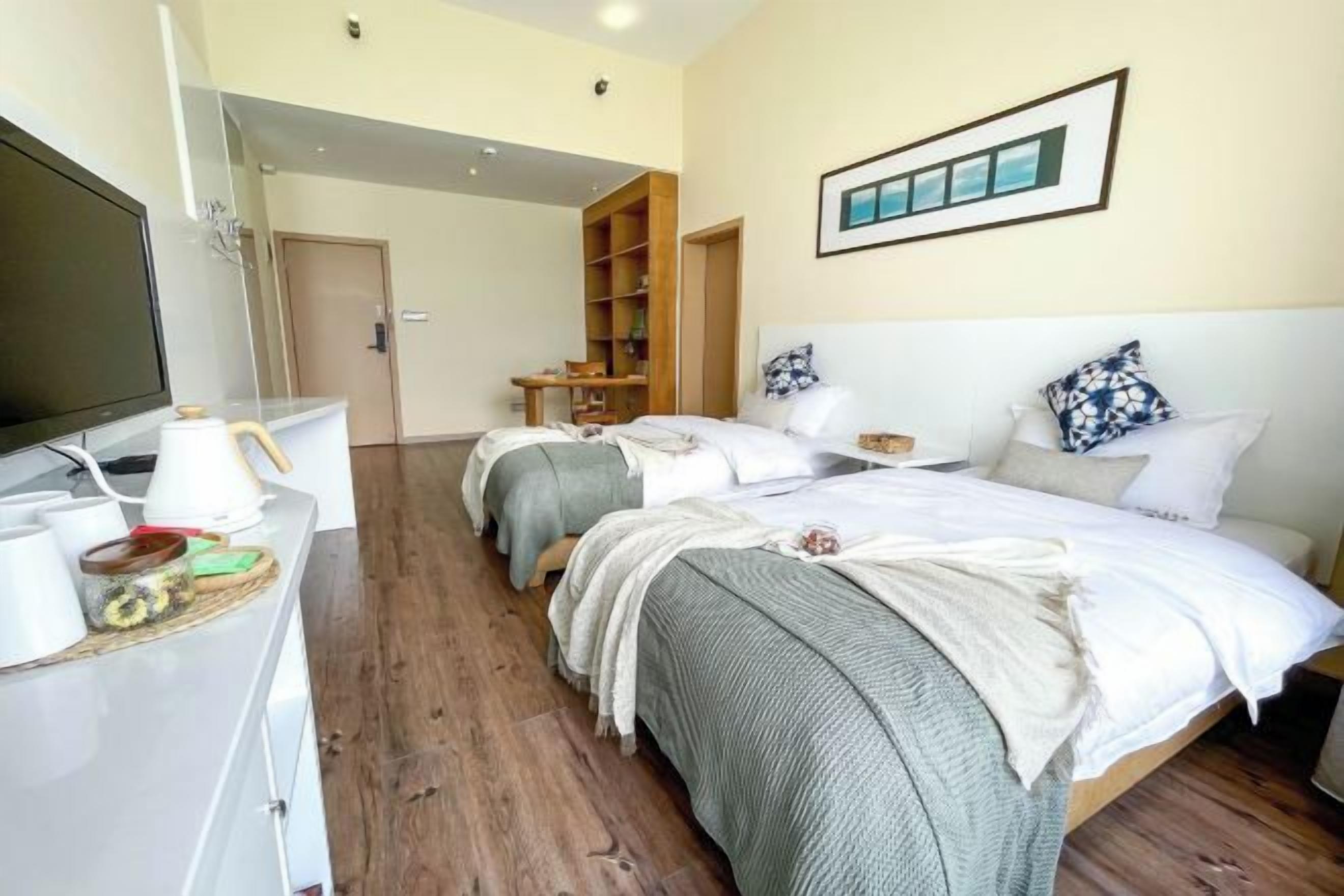 Habitación de hotel con televisión, escritorio con hervidor, dos camas, armario y estantería.