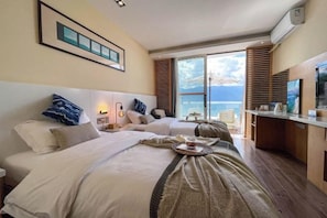 Ein Hotelzimmer mit zwei Betten, einem Fernseher, einem Schreibtisch und Meerblick.