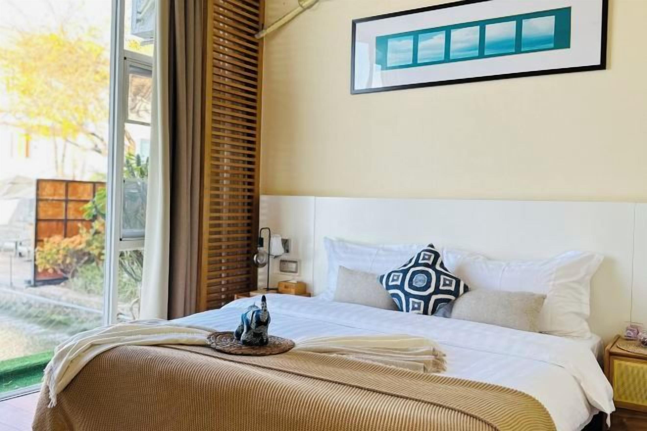 Una habitación de hotel con una cama, una ventana con persianas, una mesita de noche y un cuadro en la pared.