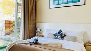 Una habitación de hotel con una cama, una ventana con persianas, una mesita de noche y un cuadro en la pared.