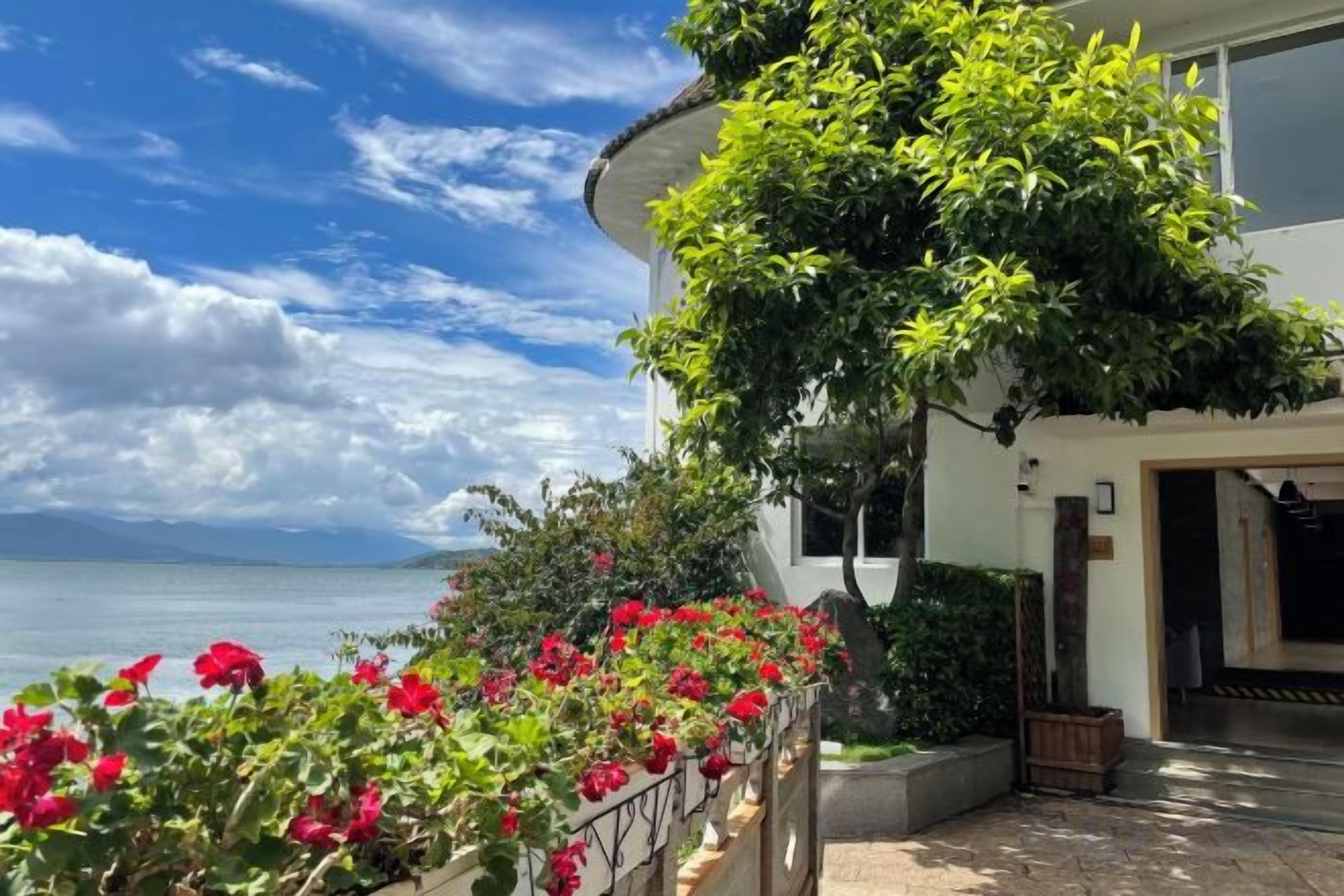Un edificio con fachada curva, un balcón con flores rojas y vista al mar.