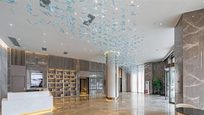 A spacious lobby with a reception desk, bookshelves, a large column, and a seating area. - Rezen Hotel Meiyo (Suining)