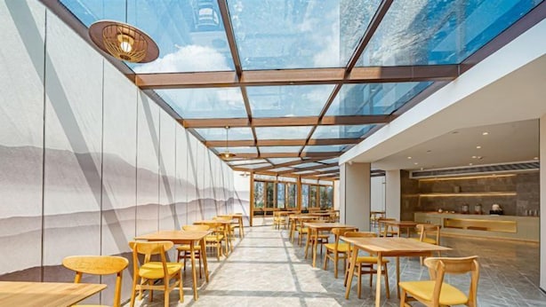 A spacious indoor area with long tables and chairs, a glass ceiling, and a view of the sky. - Rezen Hotel Meiyo (Suining)