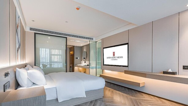 A modern hotel room with a large bed, a television, and a herringbone-patterned floor. - Rezen Hotel Meiyo (Suining)