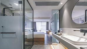 A modern hotel room with a glass partition, a large bed, a separate bathroom with a bathtub, and a large mirror. - Rezen Hotel Meiyo (Suining)