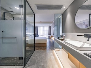 Una habitación de hotel moderna con separador de vidrio, una cama grande, baño independiente con bañera y un espejo amplio.