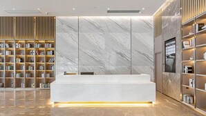 A modern reception area with marble walls, a reception desk, and bookshelves. - Rezen Hotel Meiyo (Suining)