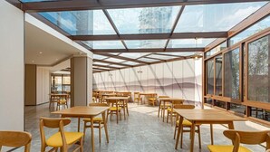 A spacious dining area with multiple tables and chairs, a glass ceiling, and large windows. - Rezen Hotel Meiyo (Suining)