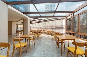 Un comedor amplio con varias mesas y sillas, techo de cristal y ventanas grandes.