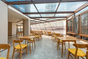 A spacious dining area with multiple tables and chairs, a glass ceiling, and large windows. - Rezen Hotel Meiyo (Suining)