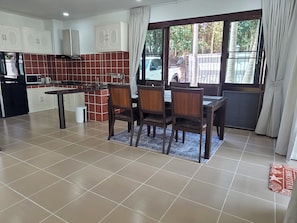 A kitchen with a dining area, featuring a tiled floor, cabinets, a stove, and a window with curtains. - Peaceful & Spacious 2-Bedroom Villa with Large Garden in Central Chaweng (Bophut koh samui)