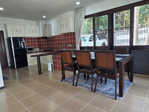 A dining area with a table and chairs, a kitchen with cabinets and appliances, and a view of the outside through a window. - Peaceful & Spacious 2-Bedroom Villa with Large Garden in Central Chaweng (Bophut koh samui)