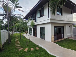 A modern two-story house with a paved walkway, palm trees, and a statue. - Peaceful & Spacious 2-Bedroom Villa with Large Garden in Central Chaweng (Bophut koh samui)