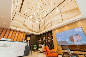 A hotel lobby with a reception desk, seating area, and a television screen displaying a welcome message. - Magnotel (Jiaxing)