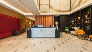 Um saguão de hotel com balcão de recepção, área de estar e uma parede decorativa com vasos.