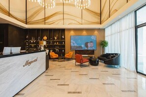 Un vestíbul d'hotel amb taulell de recepció, zona de seients i una gran pantalla de televisió.