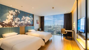 Quarto de hotel com duas camas, uma escrivaninha, uma cadeira, uma televisão e uma janela grande com vista para a cidade.