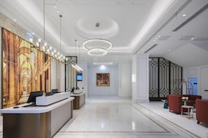A hotel lobby with a reception desk, a chandelier, a large painting, and a seating area with red sofas. - Vienna International Hotel (Nanping)