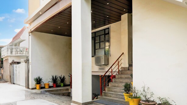 Entrada de um edifício com varanda coberta, escadas e plantas em vasos.