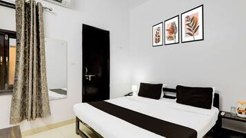 Habitación de hotel con una cama, una mesita de noche con lámpara, un teléfono y un cuadro de una planta en la pared.