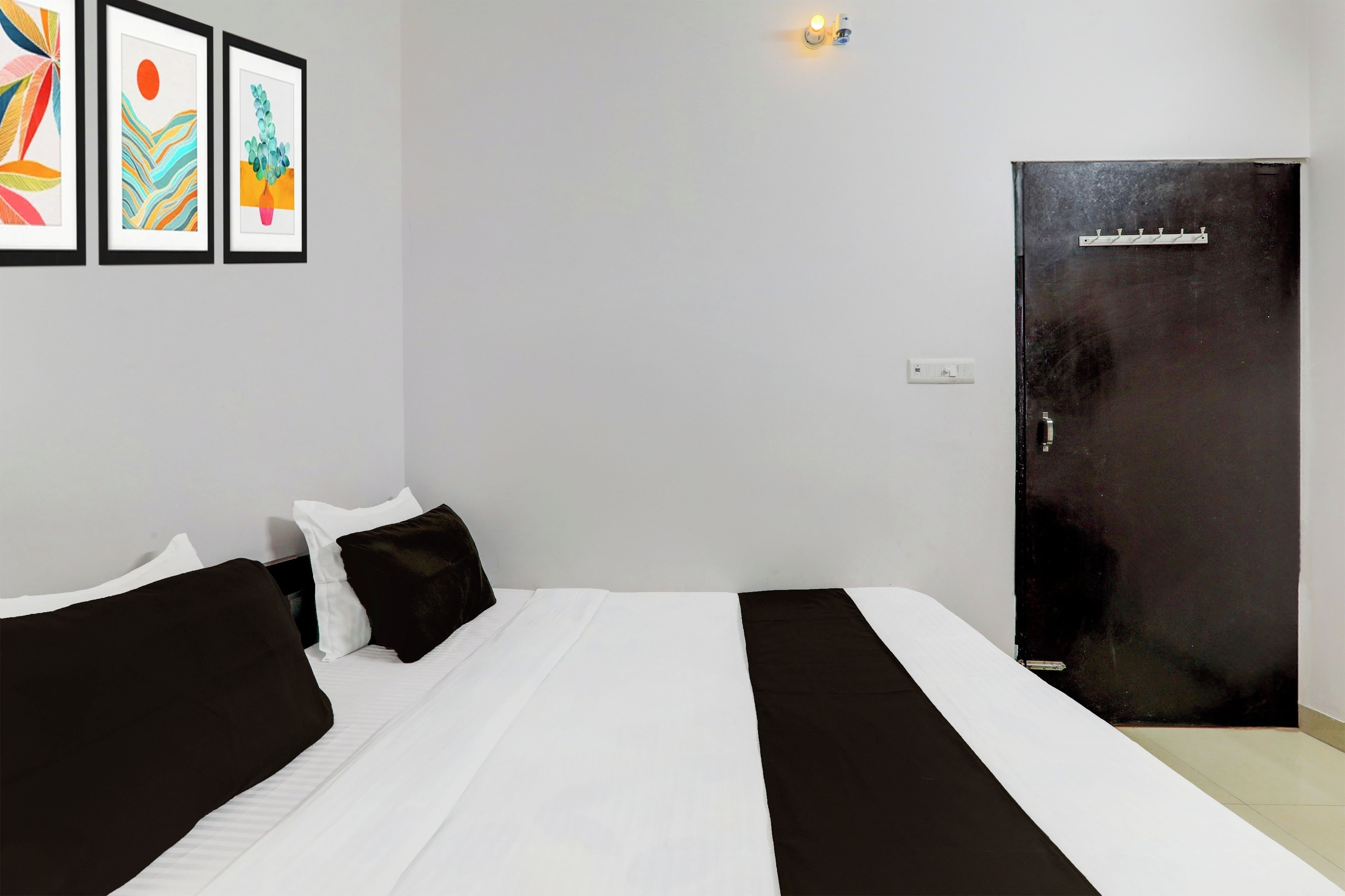 A hotel room with a bed, two pillows, a nightstand, a wall-mounted light, and a door.