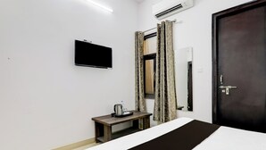 Quarto de hotel com uma cama, uma mesinha com chaleira e bandeja, uma TV fixada na parede e uma porta com espelho.