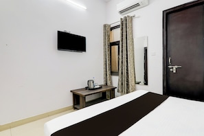A hotel room with a bed, a small table with a kettle and a tray, a TV mounted on the wall, and a door with a mirror. - Super OYO Hotel O Indira Nagar (Lucknow)