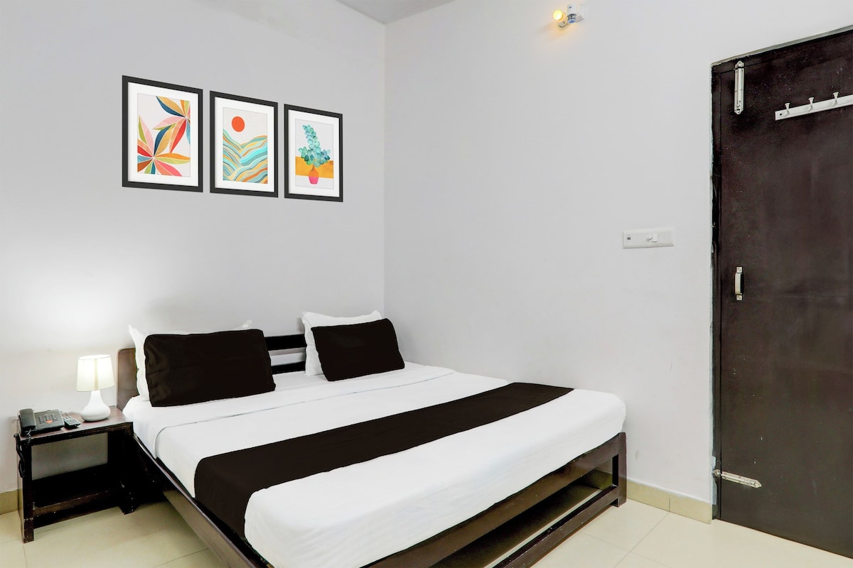 A hotel room with a bed, bedside table, lamp, and three framed artworks on the wall.
