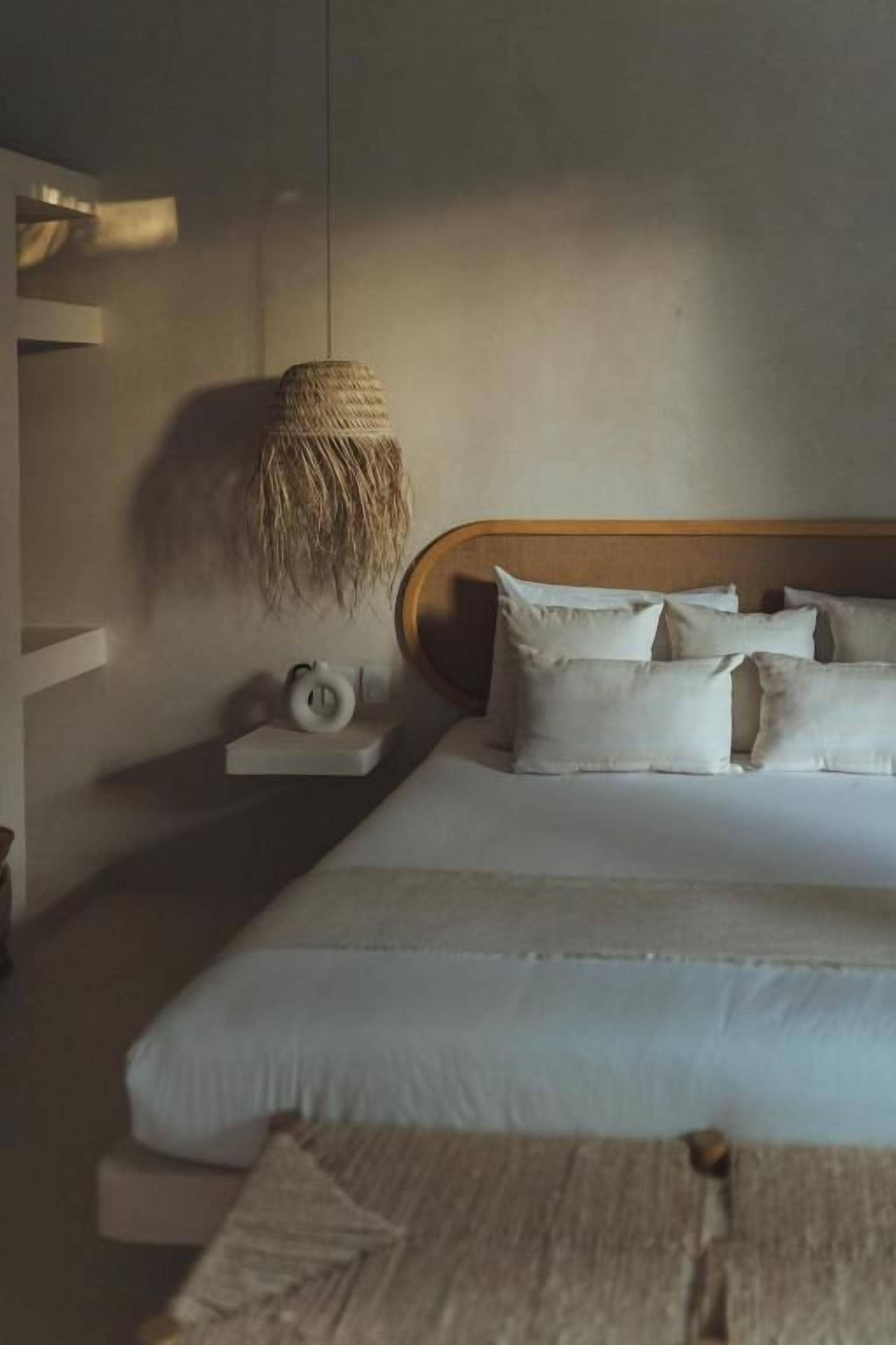 A bedroom with a bed, pillows, a bedside table, and a hanging light fixture.