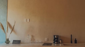 A room with a wooden counter, a coffee maker, a bottle, and a small table. - Casa Peregrino Holbox (Isla Holbox)