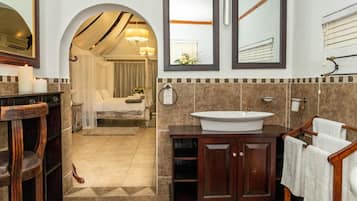 A bathroom with a large mirror, a sink, and a vanity. There is a wooden chair and a towel rack.