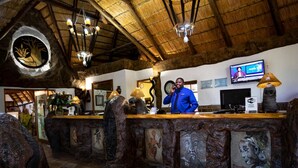 A rustic interior with a wooden reception desk, a television mounted on the wall, and a ceiling with exposed beams. - Bolivia Lodge (Polokwane)