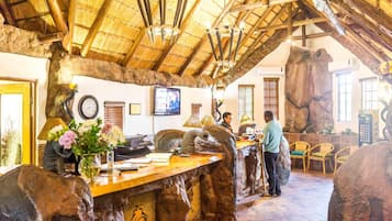 A rustic interior with a wooden ceiling, a reception desk, and a large rock feature.
