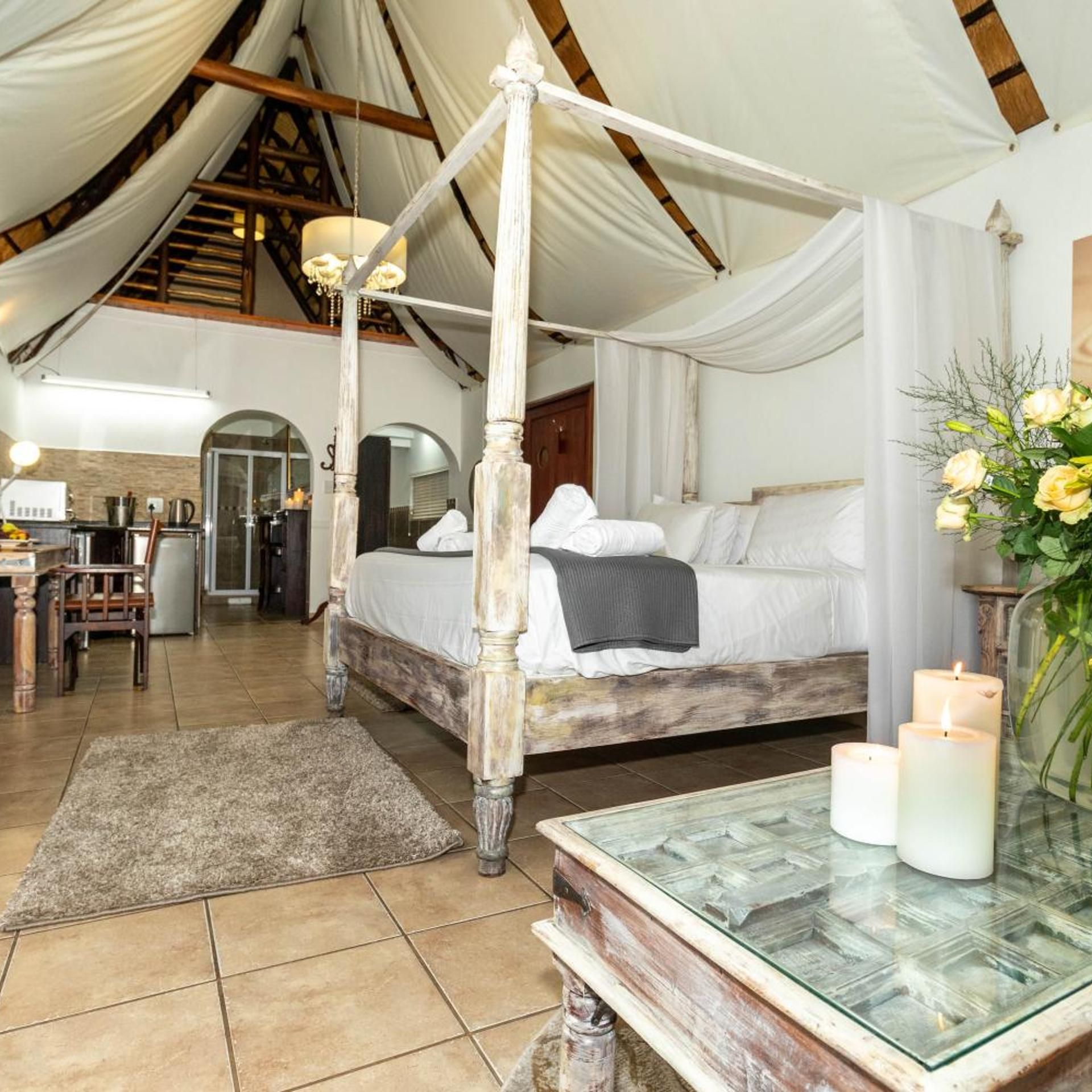 A four-poster bed with a canopy, a dining table with candles, and a kitchen area visible in the background.