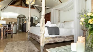 A four-poster bed with a canopy, a dining table with candles, and a kitchen area visible in the background.
