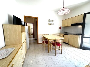 Eine kleine Küche mit Essbereich, Holzschränken, einem Kühlschrank und einer Pendelleuchte.