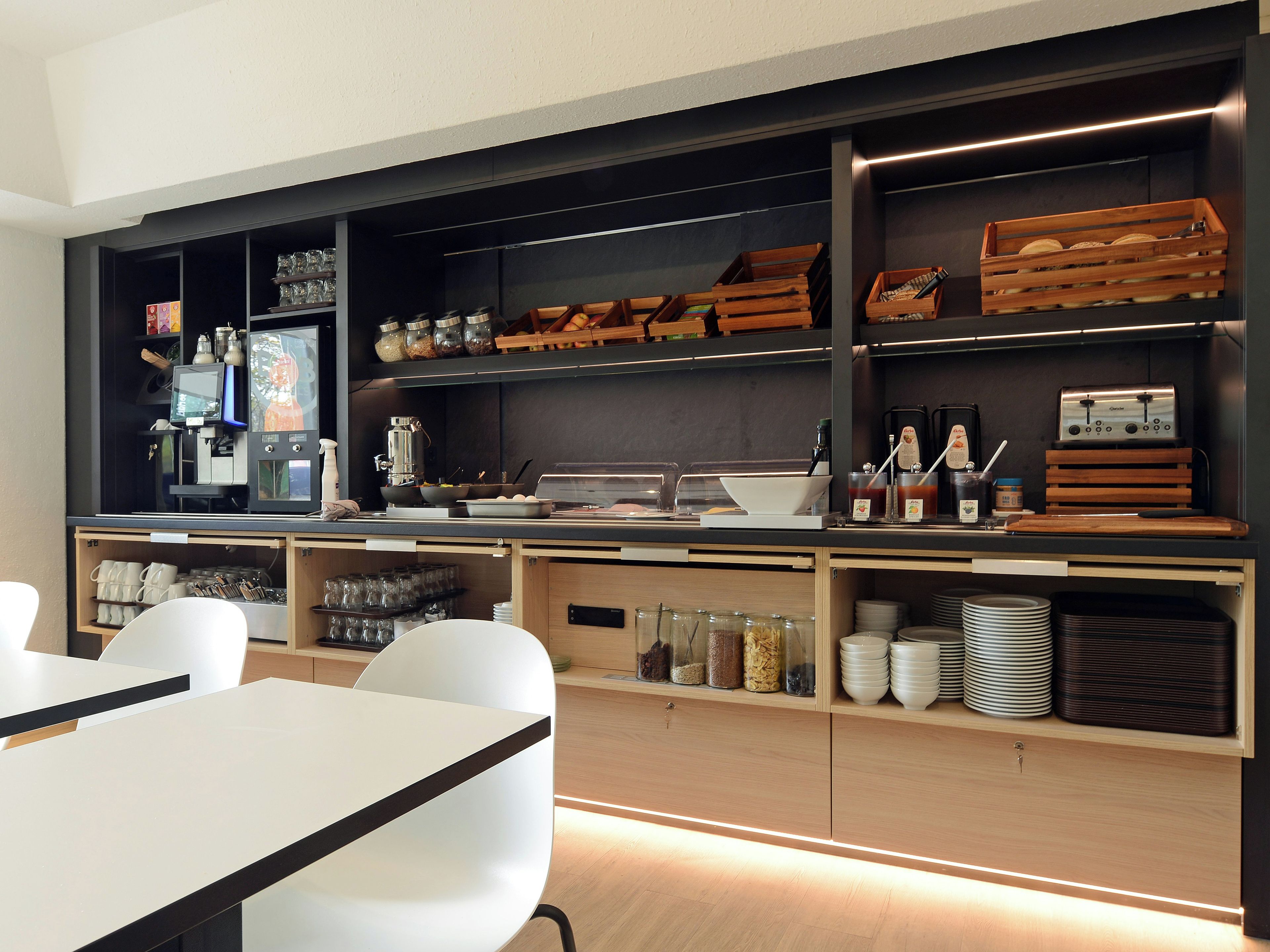 A modern kitchen with built-in appliances, wooden shelves, and a dining area with white chairs.