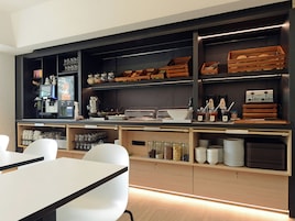 Una cocina moderna con electrodomésticos integrados, estantes de madera y un comedor con sillas blancas.