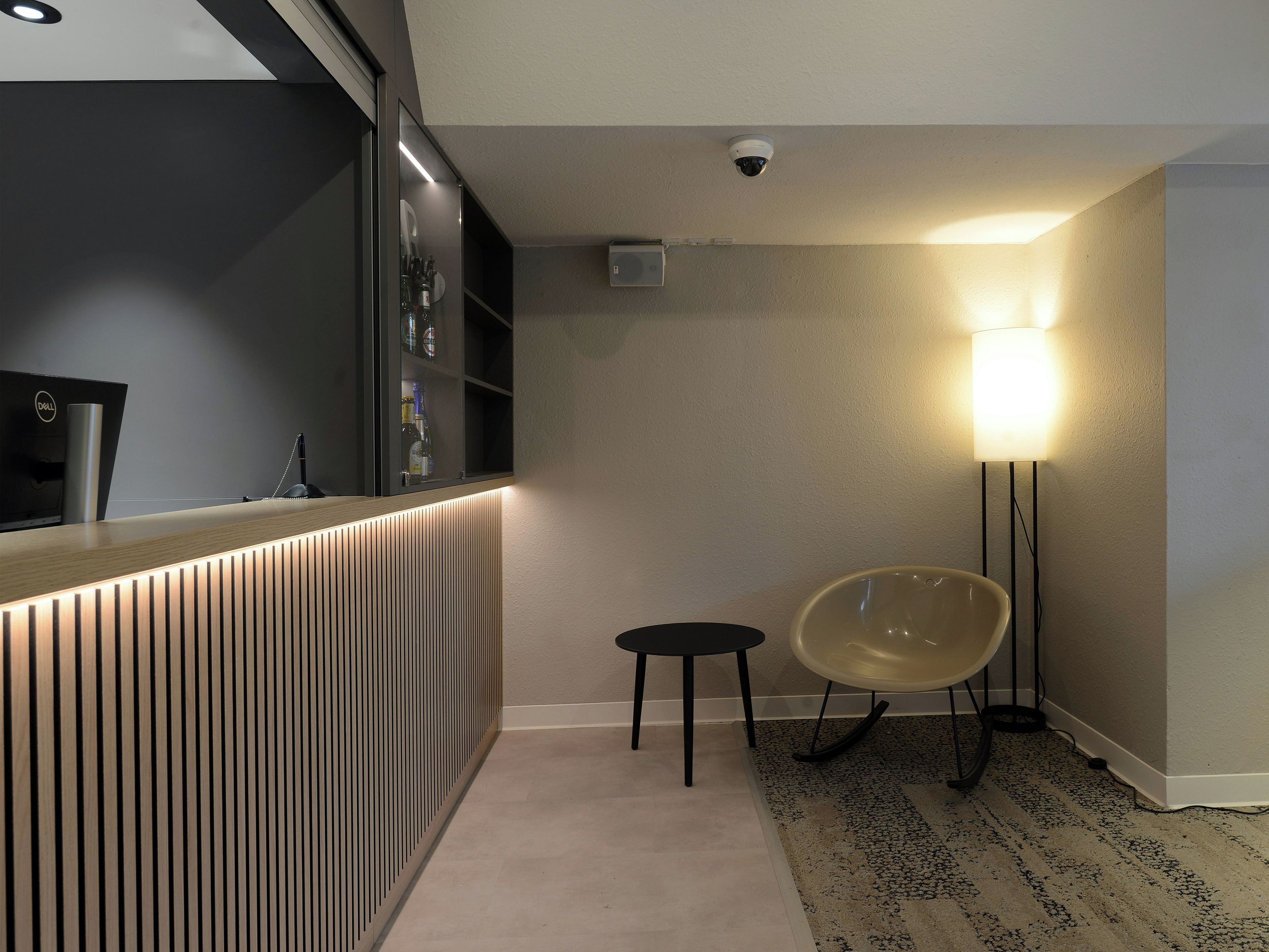 A modern hotel room with a reception desk, a security camera, a lamp, and a chair.