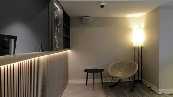 A modern hotel room with a reception desk, a security camera, a lamp, and a chair.