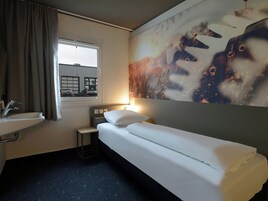 Quarto de hotel com cama, mesa de cabeceira pequena, pia e janela com cortinas.