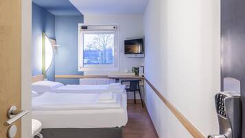 A hotel room with a bed, a desk with a chair, a television, and a window with a view of trees.
