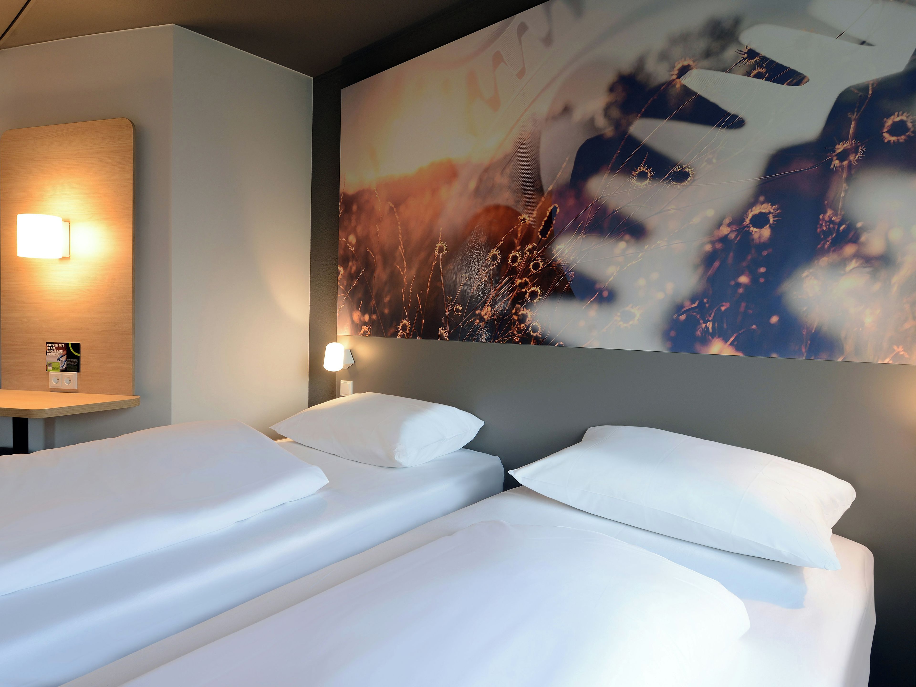 A hotel room with two beds, a wall-mounted light, and a large abstract painting.
