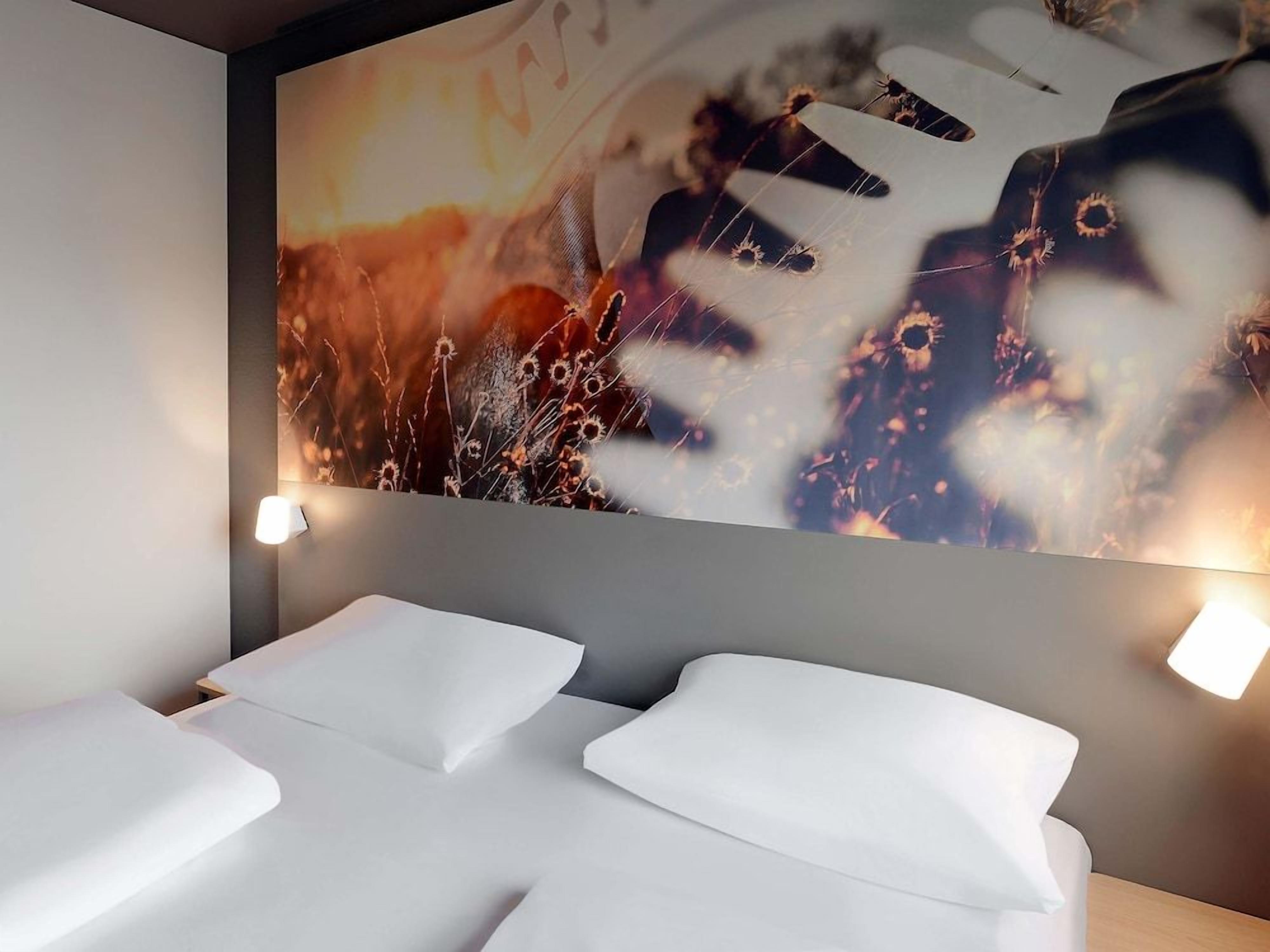 A hotel room with a large abstract painting on the wall, a bed with white linens, and two bedside tables with lamps.