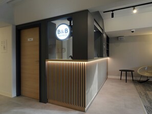 A reception desk with a B&B Hotels sign, a private room door, and a small table with a chair. - Ibis Budget Duesseldorf Willich (Willich)