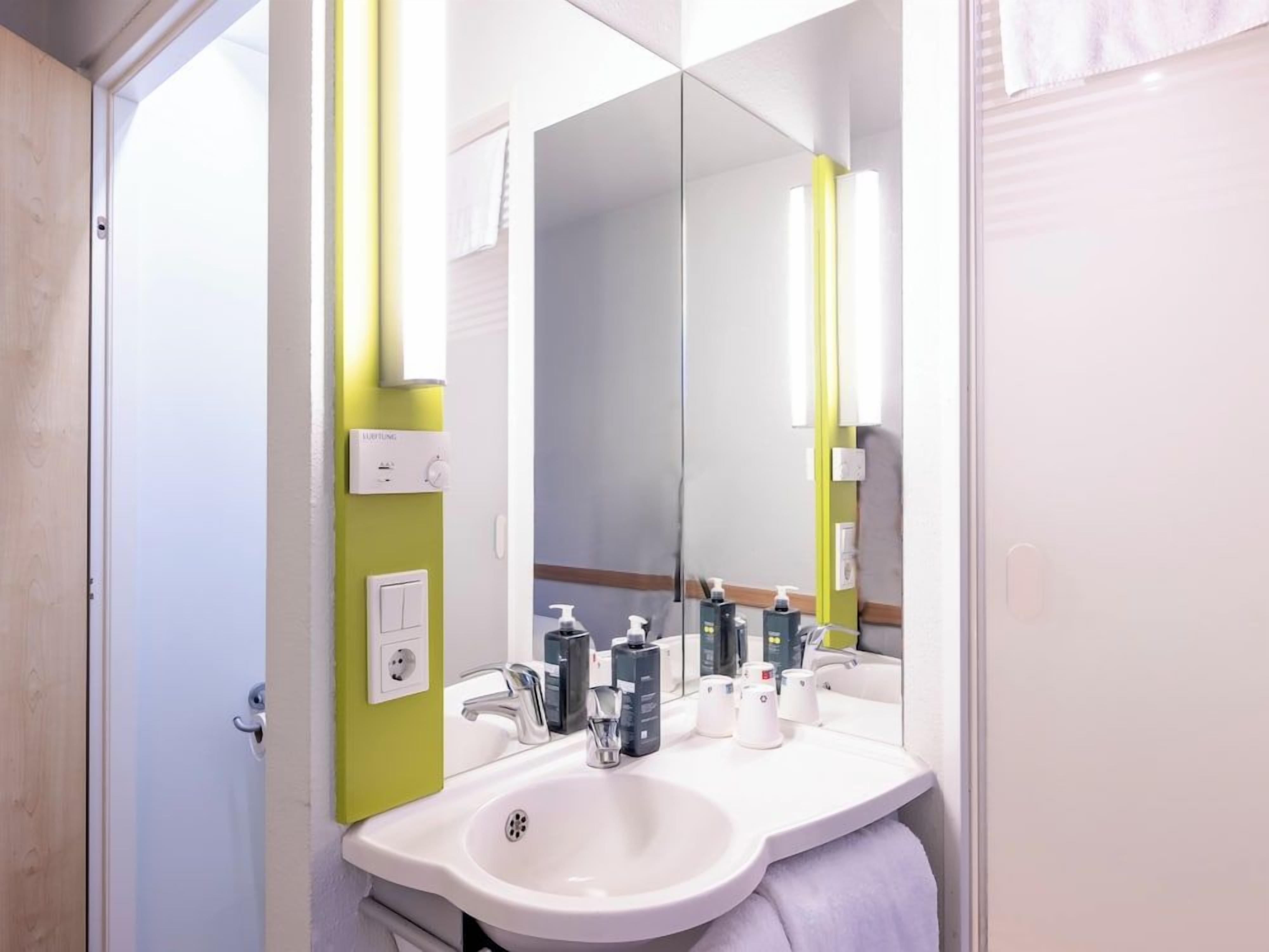A bathroom with a white sink, mirror, and green wall.
