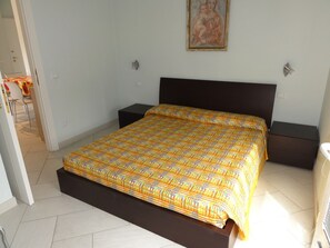A bedroom with a bed, nightstands, a painting on the wall, and a chair in the adjacent room. - Central Apartment With Parking (San Michele al Tagliamento)